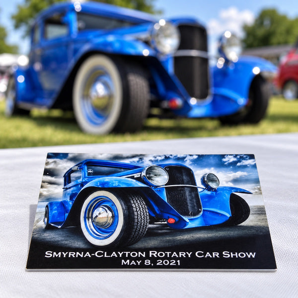 Aluminum dash plate JUV106 on a car-show table with a blue vintage car in the background.