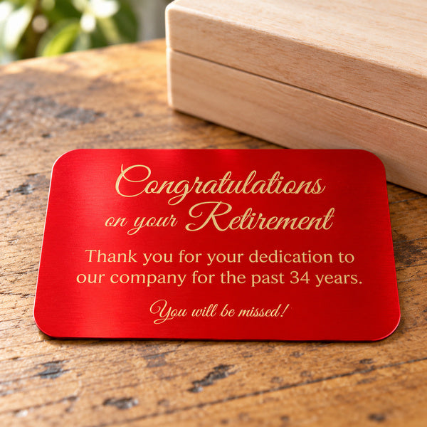 Red metal plate with gold retirement engraving beside a wooden keepsake box.